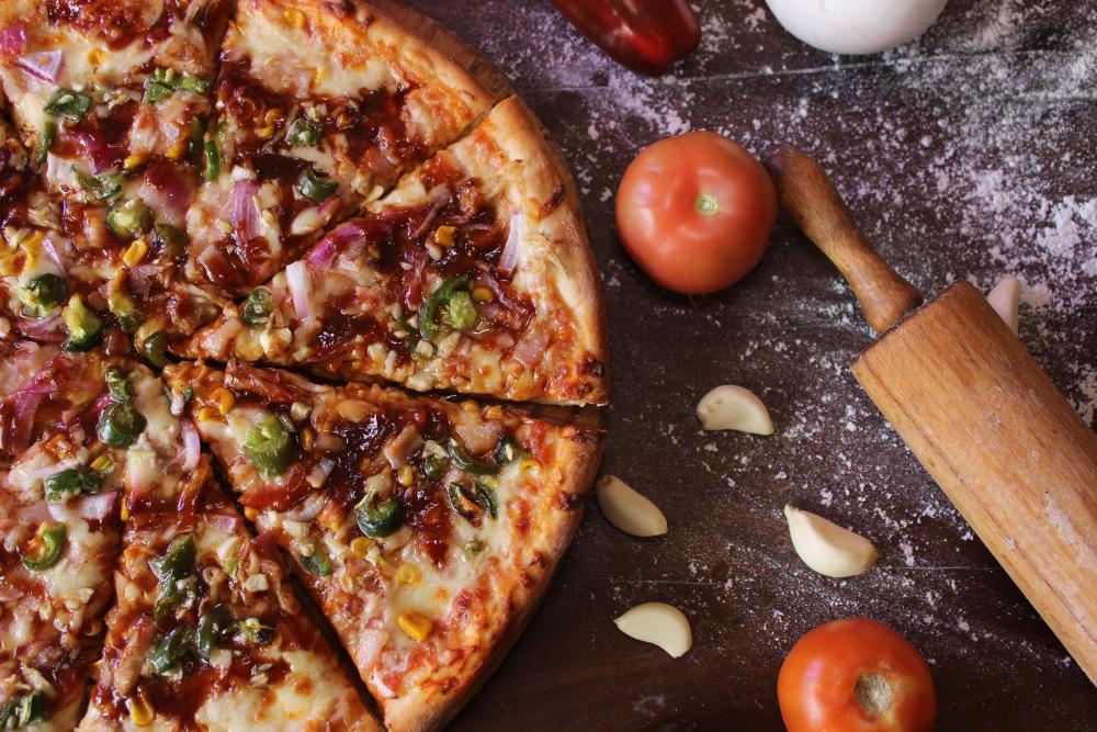 pizza, tomat, vitlöksklyftor och en brödkavel på ett mjölat bakbord